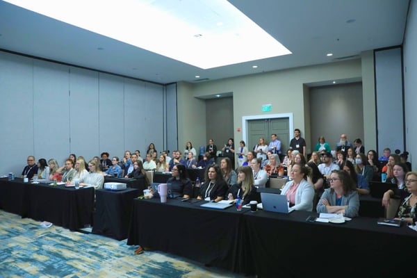 Conference attendees seated in a workshop session, watching a presentation at the front of the room.