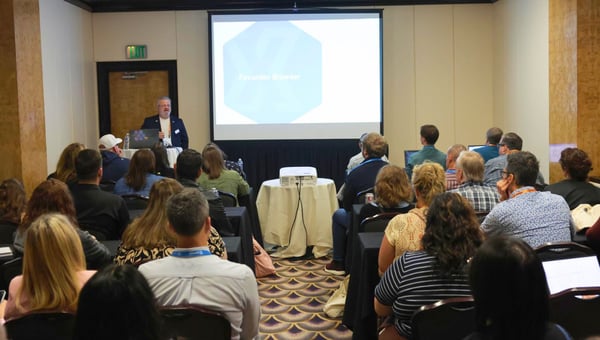 A presenter speaking to a full breakout room with slides on the screen
