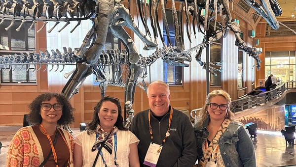 Four attendees smiling in front of dinosaur skeletons at the Cincinnati Museum Center