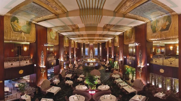 Ornate Art Deco dining hall at the Hilton Cincinnati Netherland Plaza, featuring gold ceiling murals, arched hallways, and elegant table settings.