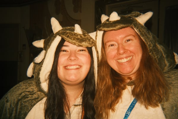 Two attendees smiling in dinosaur costume hoods