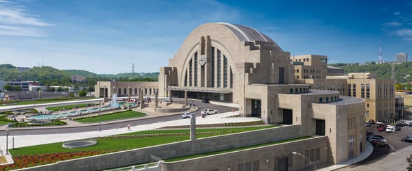 Aerial view of Cincinnati Union Terminal, a historic Art Deco building with a large domed entrance, surrounded by landscaped grounds and a fountain.