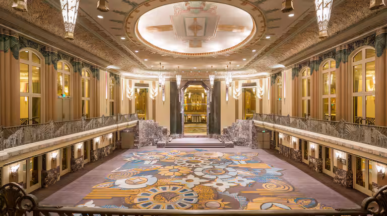Grand Art Deco ballroom hallway at the Hilton Cincinnati Netherland Plaza, with ornate chandeliers, gold detailing, and a colorful patterned carpet.